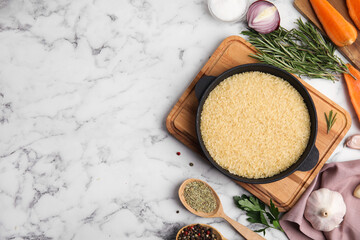Flat lay composition with dry rice in wok on white marble table. Space for text
