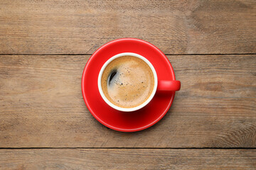 Aromatic coffee in red cup on wooden background, top view