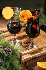 Two glasses of mulled wine and oranges on wooden tray surrounded by pine tree branches