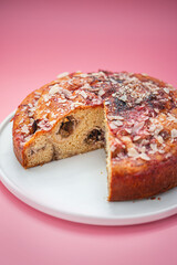 A round cake with rhubarb and almonds on a white plate on a pink surface