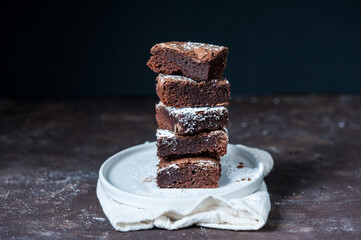 Five pieces of brownie stacked on top of each other on a white plate on a dark background