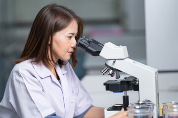 A young scientist woman in a laboratory coat looking through a microscope in a laboratory to do research and experiment. Scientist working in a laboratory. Education stock photo