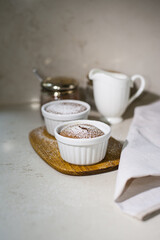 Two muffins in white ribbed baking forms on a wooden board on a marble table