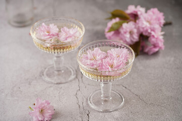 Obraz na płótnie Canvas Two champagne glasses and pink cherry blossom on a grey surface
