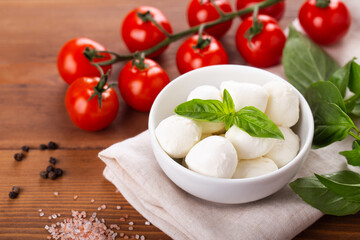 ingredients for caprese salad, mozzarella balls, cherry tomatoes on a branch, fresh basil, spices on a wooden background, horizontal