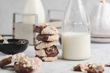 Almond half-chocolate biscuits sprinkled with chopped peanuts and placed on top of each other and milk bottle on light background