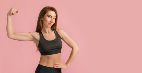 Fototapeta na wymiar Fitness girl smiling in black sportswear on a pink background. Slim woman with a beautiful athletic body and tanned skin