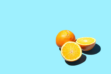A half of an orange with hard light shadow on a blue surface, two pieces and a whole orange , a template