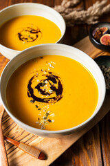 Two grey bowls with pumpkin cream soup with pumpkin seed oil on wooden table