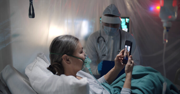 Doctor in ppe uniform working with corona virus infected patient watching family photo on smartphone