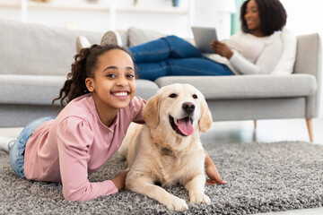 Young afro girl having fun with dog at home