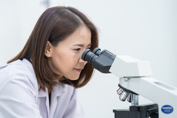 Fototapeta premium A young scientist woman in a laboratory coat looking through a microscope in a laboratory to do research and experiment. Scientist working in a laboratory. Education stock photo