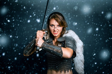Portrait of a medieval woman warrior in chain mail and fur with a sword in her hands posing while...