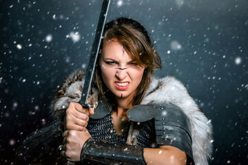 Portrait of a medieval woman warrior in chain mail and fur with a sword in her hands posing while...