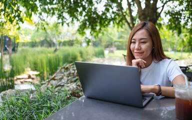A young asian woman using and working on laptop while sitting in the park