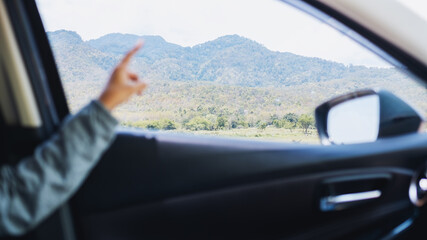 Fototapeta na wymiar A young woman pointing finger at the mountains view while riding in a car