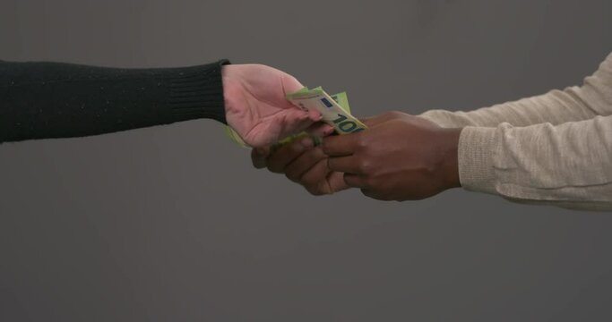 Unrecognizable African man with bundle of 100 euro banknotes. Male offering one bill. Caucasian woman's hand takes all the rest of money. Isolated on grey background