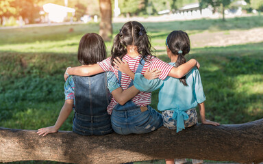 Children friendship concept with happy girl kids in the park having fun sitting under tree shade...