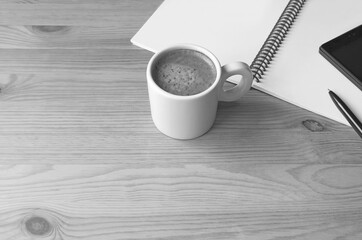 Cup of Hot Coffee with a Note and Cellphone on Wooden Working Desk in Monochrome