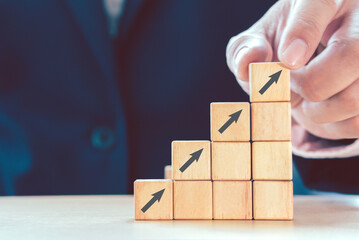 Hand of businessman arranging wood cube with arrow symbol stacking as growth step stair. Growth successful and target concept.