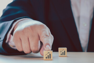 Close up businessman hand choose arrow above bar graph growth to success process and blurred the arrow above bar graph icon on wooden cube. Business and satisfaction concept.