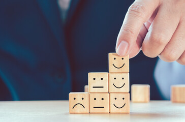 Hand of businessman arranging smiley face and sad or bad face symbol icon on wood cube as stair step shape. Business growth and management concept.