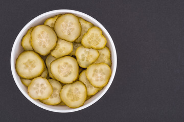 White glass bowl of sliced salted cucumber. Isolated on a dark grey background. Top view close up