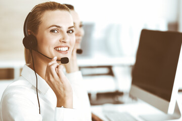 Blond female customer service representative and her colleague are consulting clients online using headset. Call center and business people concept