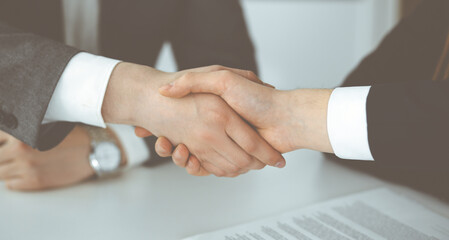 Unknown businessman shaking hands with his colleague or partner above the glass desk in modern office, close-up. Business people group at meeting