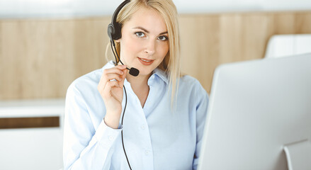 Blonde business woman sitting and communicated by headset in call center office. Concept of telesales business or home office occupation