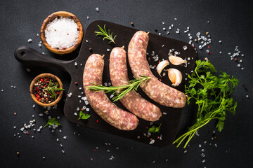 Bratwurst or sausages on cutting board with spices at black table.