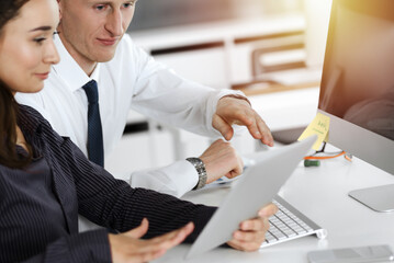 Business woman and man discussing questions while using computer at workplace in sunny office