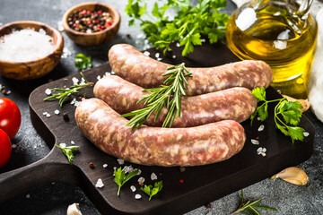 Bratwurst or sausages on cutting board with spices at black table.