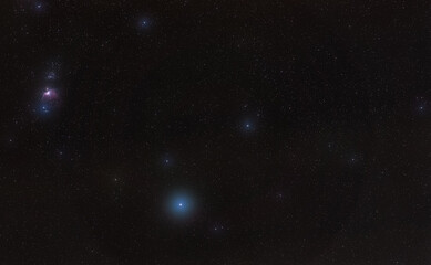 Winter night sky with purple Orion nebula, bright blue Rigel star - diffused through some clouds -...