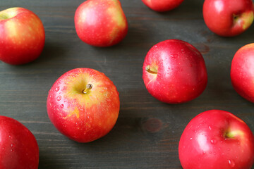 Closeup red fresh ripe apples with water droplets scattered on dark brown wooden table		