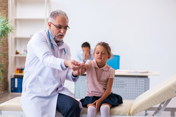 Obraz premium Small girl with her father visiting old male doctor