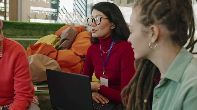 Handheld slowmo of young women sitting on floor in lounge area of start-up office and discussing projects