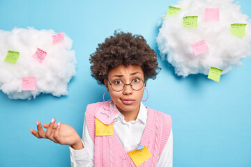 Hesitant clueless Afro American schoolgirl poses around paper stickers with written tasks to do...