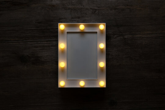 Glowing white frame with light bulbs on a vintage wooden background. Blank for postrer or postcards.