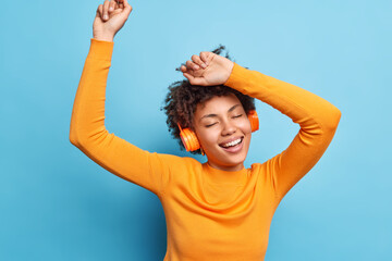 Photo of relaxed curly haired young woman keeps eyes closed dances and catches every bit of music...