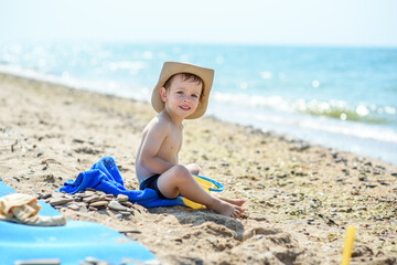 Fototapeta na wymiar A small boy alone plays on the seashore, wearing a hat and striped shorts. Heat