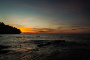 Vivid sunset sky waterscape and silhouette forest island