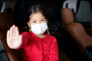 Asian child or kid girl wearing white face mask in car and raising hand for ban stop and break to If you don't wear a mask, don't get into the car or drive concept for protect covid-19 coronavirus