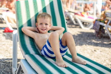 Fototapeta na wymiar a boy of 4 years old in striped shorts lies on a sunbed on the beach, contented and happy. Summer, seashore