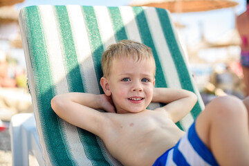 Fototapeta na wymiar a boy of 4 years old in striped shorts lies on a sunbed on the beach, contented and happy. Summer, seashore