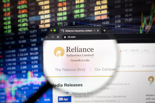 Reliance Industries Limited company logo on a website with blurry stock market developments in the background, seen on a computer screen through a magnifying glass