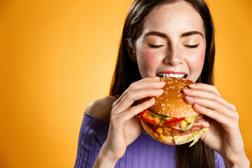 Girl bites cheeseburger with satisfaction. Woman eating delicious hambuger with pleasure and smile,...