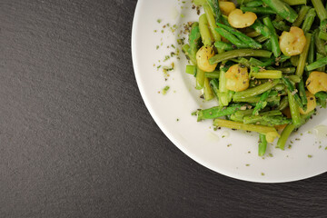 Plate of asparagus with prawns, a touch of spices and olive oil, slate stone background. Copy space.