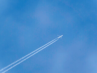 Passenger plane flies across clear blue sky leaving a jet contrail. Aircraft high in the air. Travel by plane.