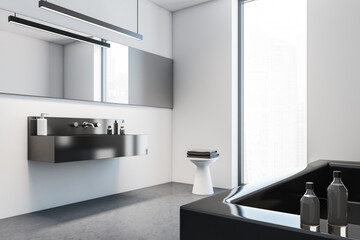 White wall with black stone sink and mirror. Modern stylish hotel bathroom interior, with square ceramic bathtub. Panoramic window.